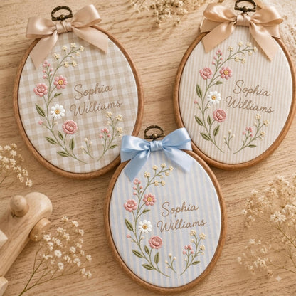 May include: Three oval wooden embroidery hoops featuring fabric backgrounds in beige gingham, white stripes, and blue stripes. Each hoop displays embroidered floral stems with pink and white flowers and the name Sophia Williams in script text.