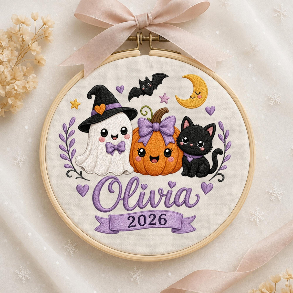 May include: A round wooden embroidery hoop containing a white fabric panel with a stitched design of a ghost in a witch hat, a pumpkin with a purple bow, and a black cat. The text Olivia and 2026 are embroidered in purple. A light pink ribbon is tied at the top.