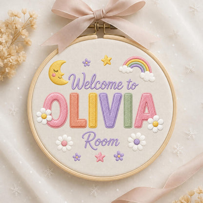 May include: A circular wooden embroidery hoop containing white fabric with the embroidered text Welcome to OLIVIA Room. The design features a yellow crescent moon, a colorful rainbow, stars, and white daisies. A light pink ribbon is tied at the top.