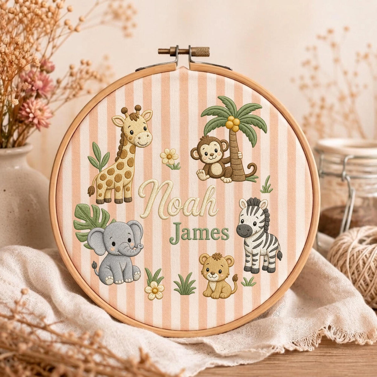 May include: A circular wooden embroidery hoop containing fabric with vertical beige and white stripes. The fabric features embroidered cartoon animals including a giraffe, monkey, elephant, zebra, and lion, with the names Noah James in the center.