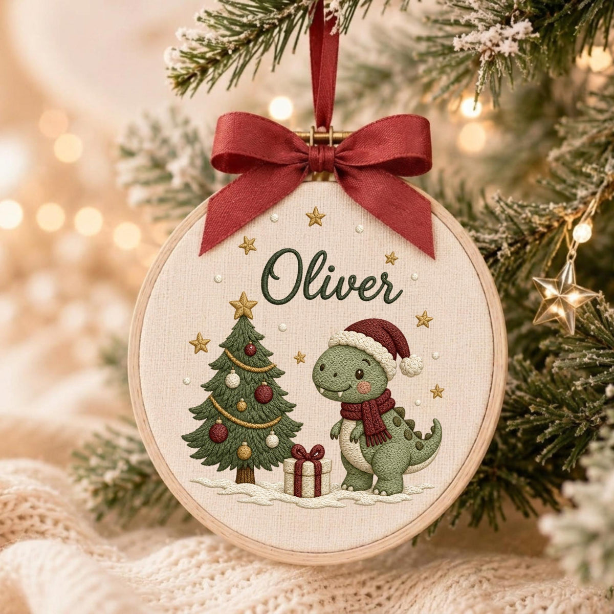 May include: A round wooden embroidery hoop ornament featuring a cream-colored fabric background. The design includes a green dinosaur wearing a red scarf and Santa hat, a decorated Christmas tree, a gift box, and the name Oliver in dark green.