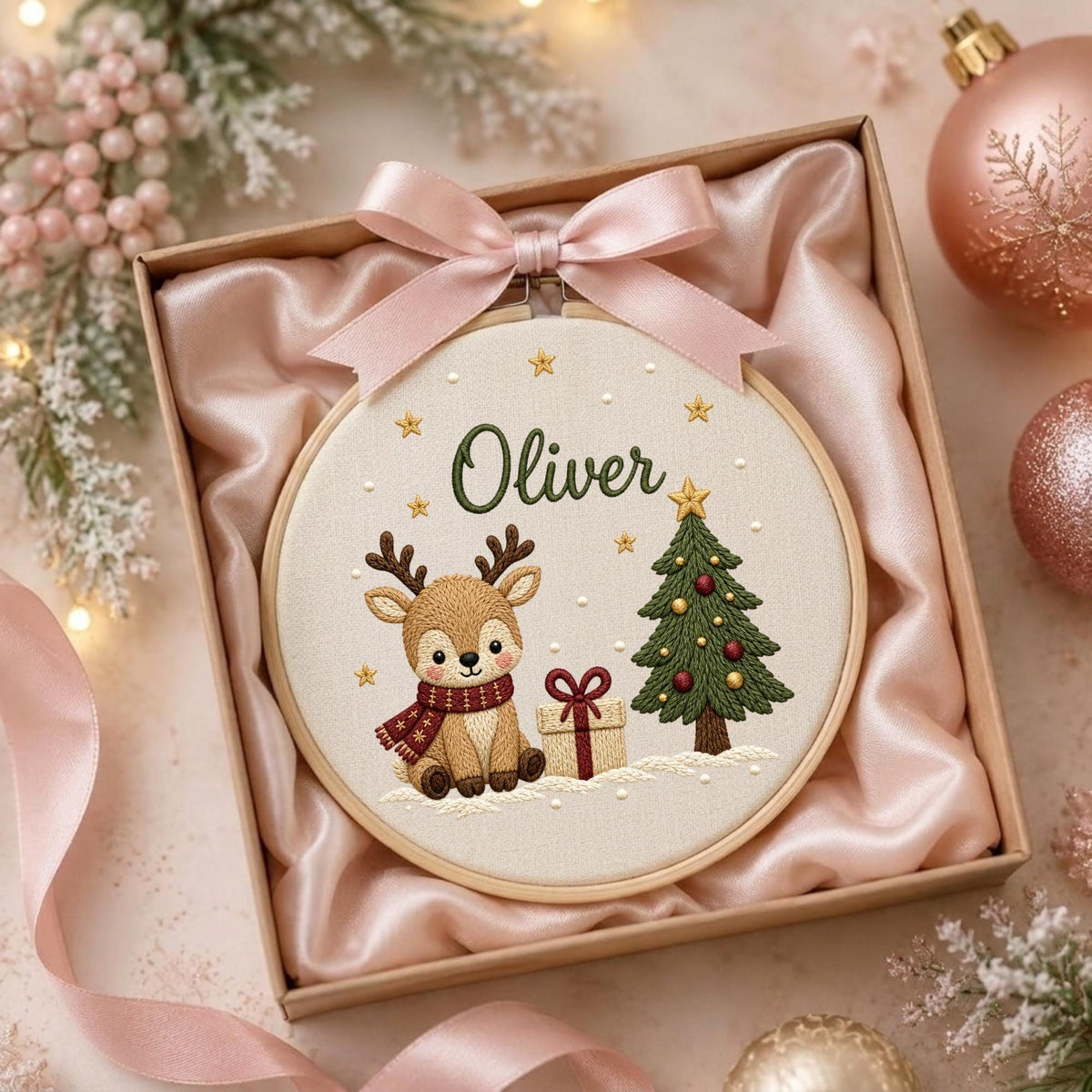 May include: A round wooden embroidery hoop containing a fabric panel with a stitched design of a reindeer wearing a red scarf, a decorated Christmas tree, and a gift box. The name Oliver is embroidered in green above the reindeer.