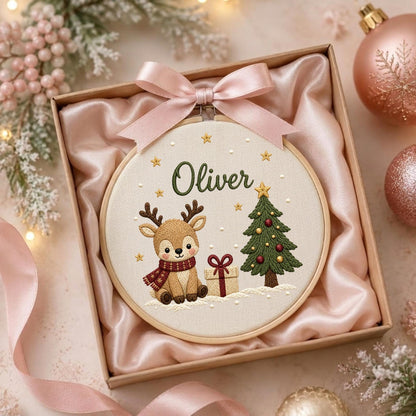 May include: A round wooden embroidery hoop containing a fabric panel with a stitched design of a reindeer wearing a red scarf, a decorated Christmas tree, and a gift box. The name Oliver is embroidered in green above the reindeer.