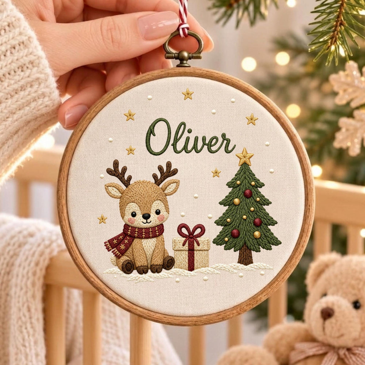 May include: A circular wooden embroidery hoop containing a cream-colored fabric panel. The embroidery features a brown reindeer wearing a red scarf, a gift box with a red ribbon, and a green Christmas tree. The name Oliver is stitched in green.