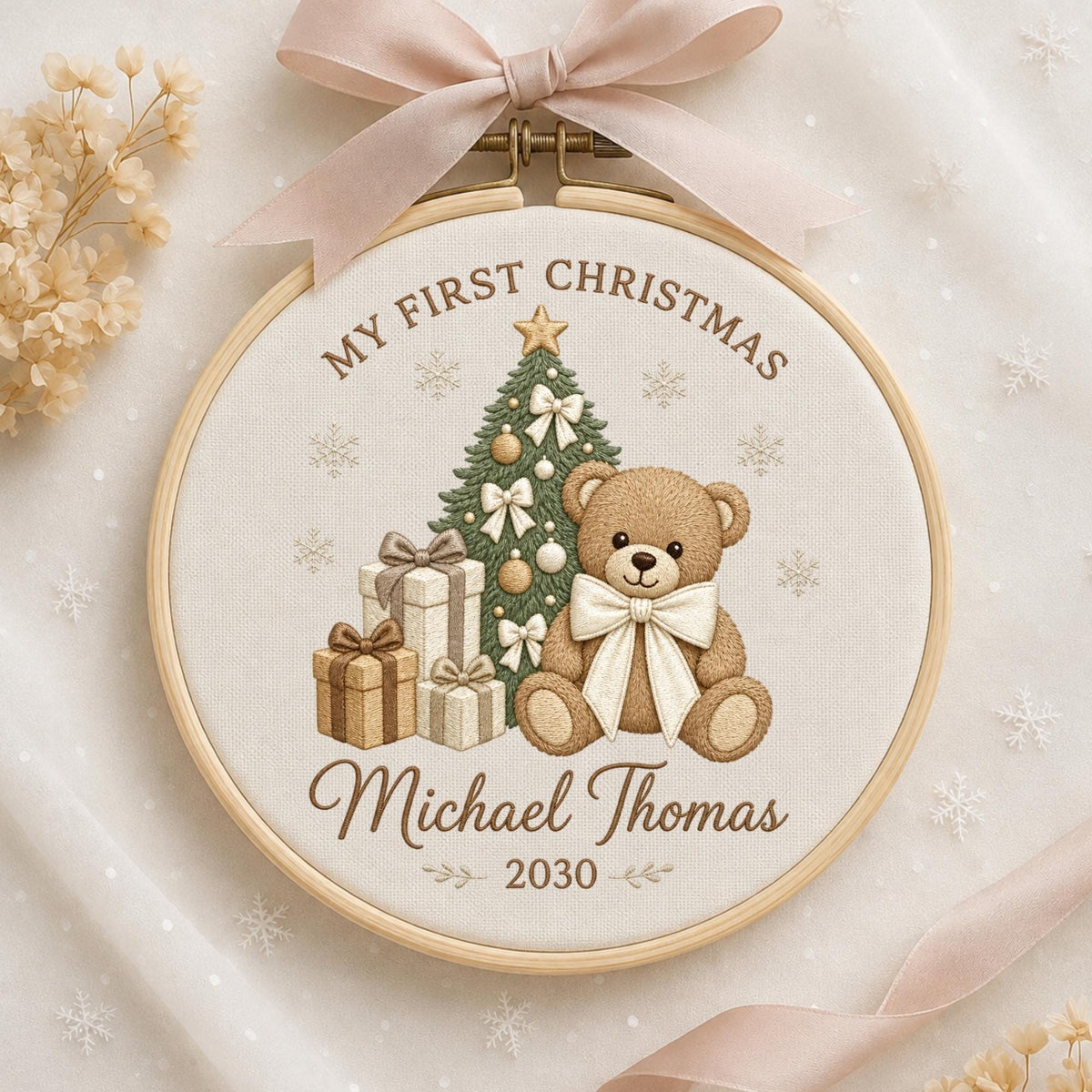 May include: A round wooden embroidery hoop featuring a beige fabric background with a brown embroidered design of a teddy bear, a Christmas tree, and gift boxes. The text reads MY FIRST CHRISTMAS, Michael Thomas, and 2030. A light pink ribbon is tied at the top.
