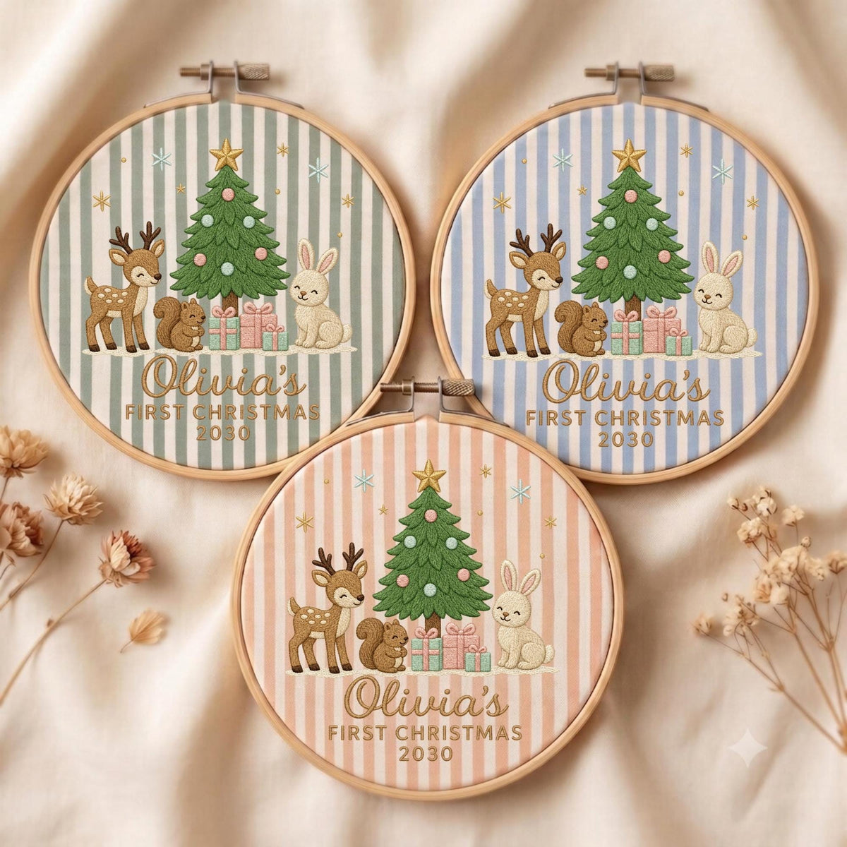 May include: Three circular embroidery hoops featuring fabric with vertical stripes in sage green, light blue, and soft peach. Each hoop displays an embroidered Christmas tree, a deer, a squirrel, a rabbit, and gifts with the text Olivia's FIRST CHRISTMAS 2030.
