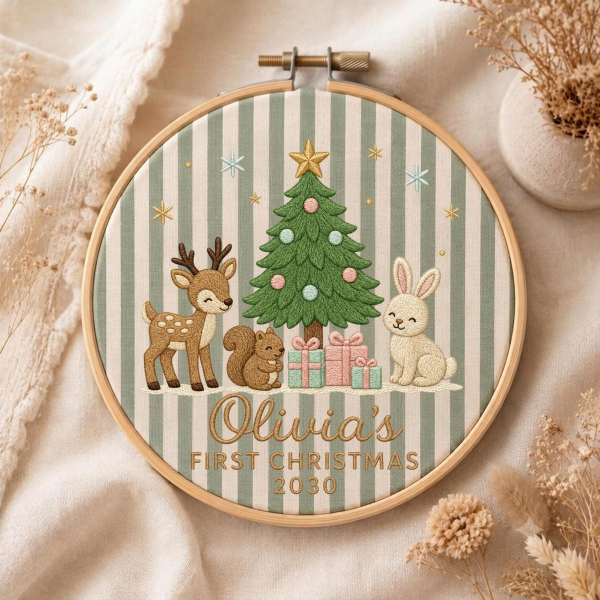 May include: A circular embroidery hoop featuring a green and white striped fabric background. The design includes a green Christmas tree, a brown deer, a brown squirrel, and a white rabbit with gifts. Text reads: Olivia's FIRST CHRISTMAS 2030.