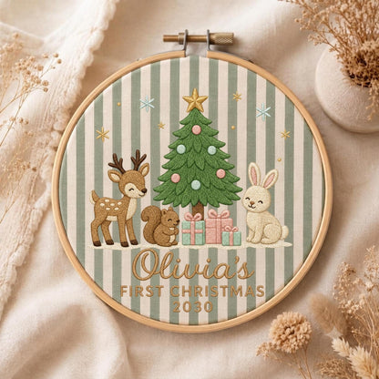 May include: A circular embroidery hoop featuring a green and white striped fabric background. The design includes a green Christmas tree, a brown deer, a brown squirrel, and a white rabbit with gifts. Text reads: Olivia's FIRST CHRISTMAS 2030.