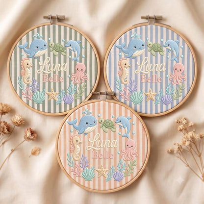 May include: Three circular wooden embroidery hoops featuring striped fabric backgrounds in sage green, light blue, and peach. Each hoop displays embroidered sea creatures including a whale, turtle, dolphin, seahorse, and octopus, with the text Luna Belle.