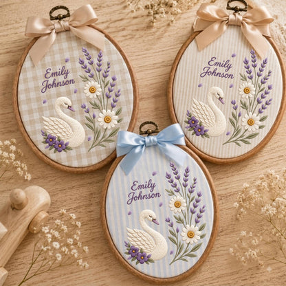 May include: Three oval embroidery hoops featuring white swans, lavender sprigs, and daisies stitched on fabric. Each hoop displays the name Emily Johnson, a decorative ribbon bow at the top, and a wooden frame. The backgrounds include gingham and stripes.