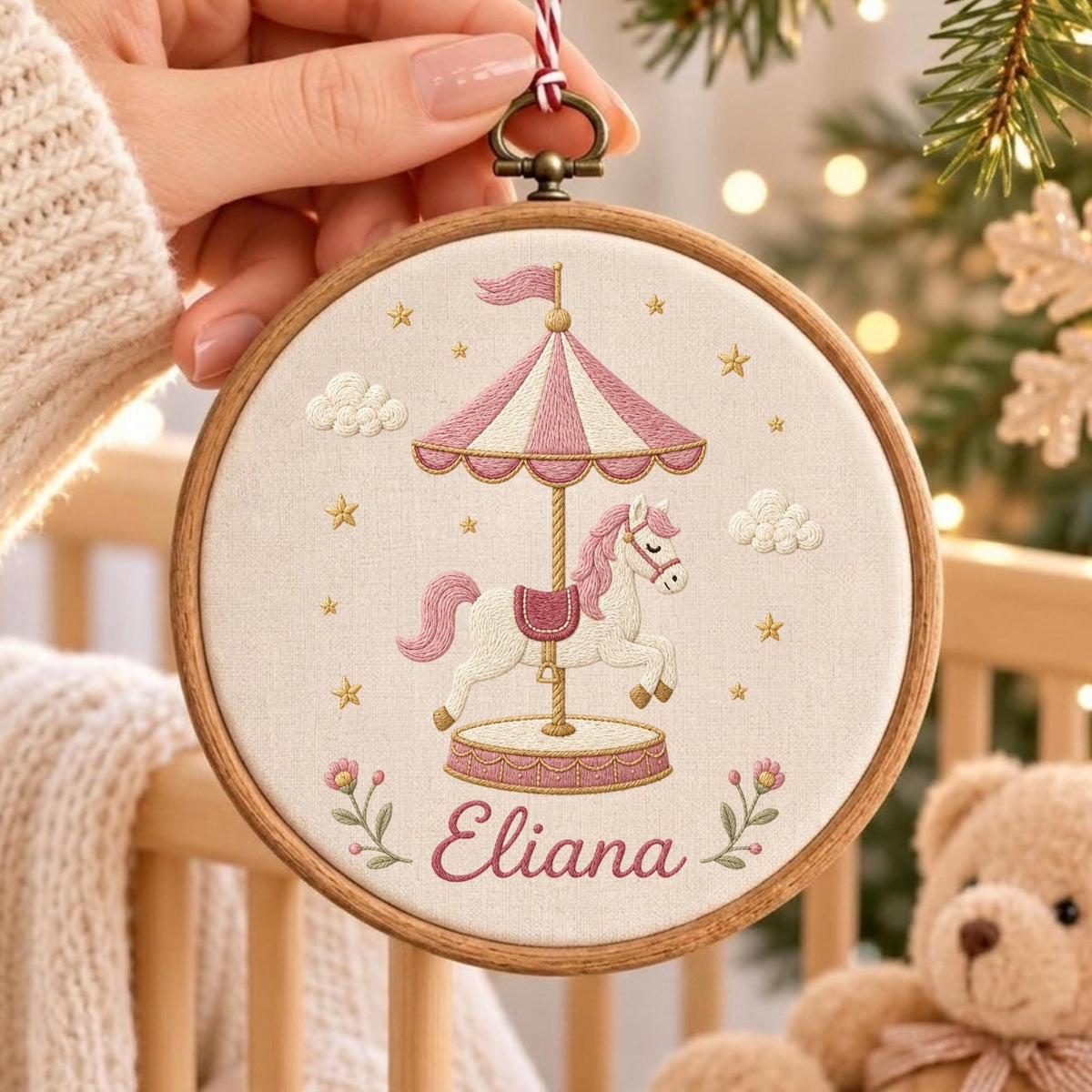 May include: A circular wooden embroidery hoop featuring a stitched carousel horse design on cream fabric. The carousel has a pink and white striped canopy, a white horse with a pink mane, and the name Eliana embroidered in pink script below.