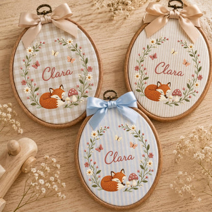 May include: Three oval embroidery hoops featuring fabric backgrounds with gingham or striped patterns. Each hoop displays the name Clara in cursive script, surrounded by a floral wreath, a sleeping fox, a mushroom, and small butterflies.