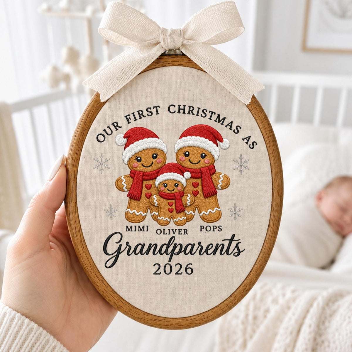May include: An oval wooden embroidery hoop containing fabric with embroidered gingerbread figures wearing red hats and scarves. Text reads: OUR FIRST CHRISTMAS AS MIMI OLIVER POPS Grandparents 2026. A beige fabric bow is attached to the top of the hoop.