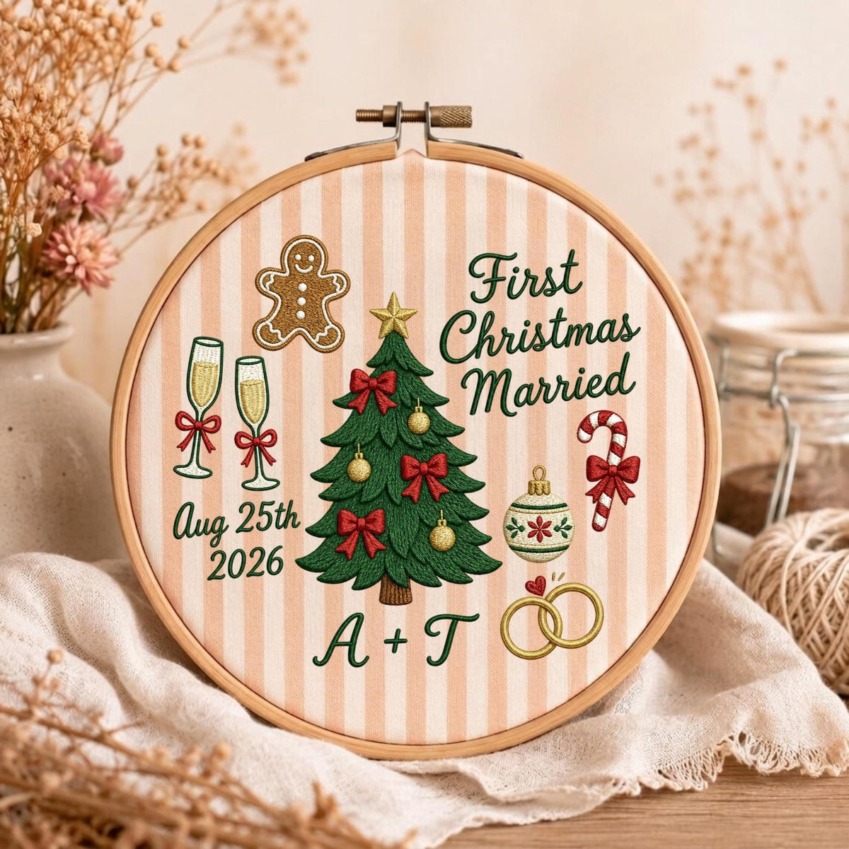 May include: A round embroidery hoop featuring a beige and white striped fabric with embroidered Christmas motifs including a tree, gingerbread man, candy cane, champagne flutes, and rings. Text reads First Christmas Married and Aug 25th 2026 A + T.