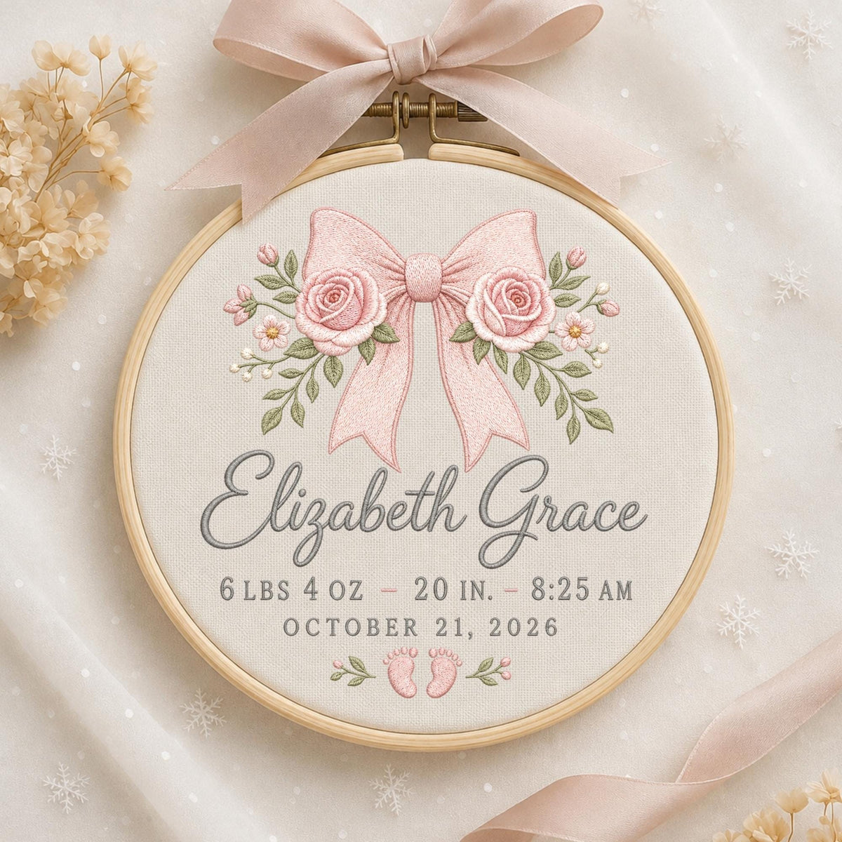 May include: A circular wooden embroidery hoop containing cream fabric with a pink ribbon and rose embroidery. The text reads Elizabeth Grace, 6 lbs 4 oz, 20 in, 8:25 am, October 21, 2026, with small embroidered baby feet at the bottom.