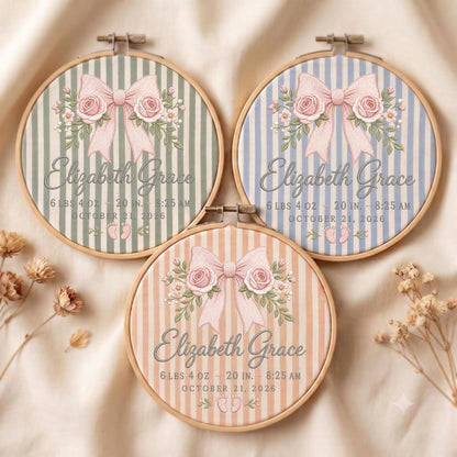 May include: Three circular wooden embroidery hoops featuring striped fabric in sage green, light blue, and peach. Each displays a pink bow with roses, the name Elizabeth Grace, birth details including 6 lbs 4 oz, 20 in, 8:25 AM, October 21, 2026, and baby footprints.