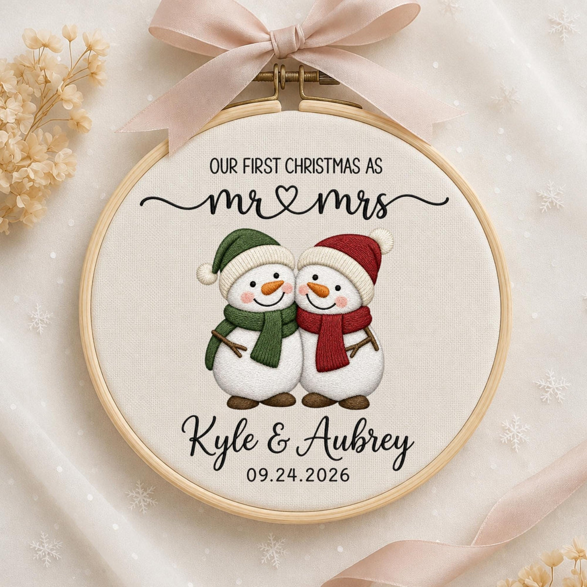 May include: A round wooden embroidery hoop containing white fabric with a printed design of two snowmen wearing green and red scarves and hats. The text reads: OUR FIRST CHRISTMAS AS mr &amp; mrs, Kyle &amp; Aubrey, and the date 09.24.2026.