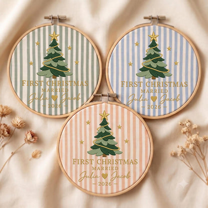 May include: Three circular wooden embroidery hoops featuring fabric with vertical stripes in sage green, light blue, and soft peach. Each hoop displays an embroidered Christmas tree with a gold star, the text FIRST CHRISTMAS MARRIED, and the names Julia and Jacob with the year 2026.