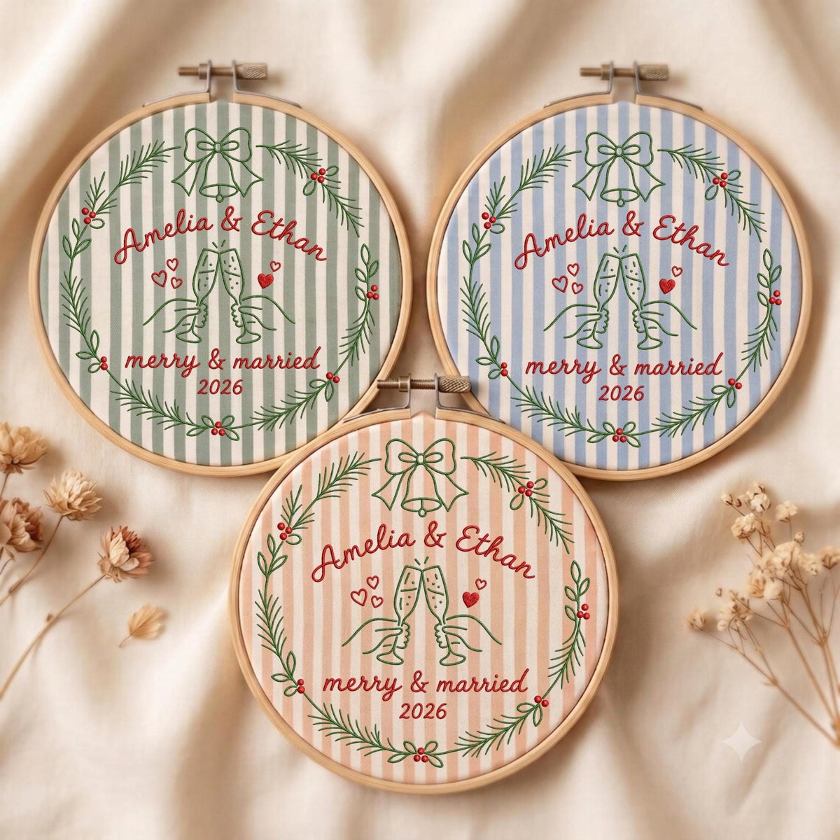 May include: Three circular embroidery hoops featuring striped fabric in sage green, light blue, and peach. Each hoop displays a green embroidered wreath with a bell, two hands clinking champagne glasses, red hearts, and the text Amelia &amp; Ethan merry &amp; married 2026.