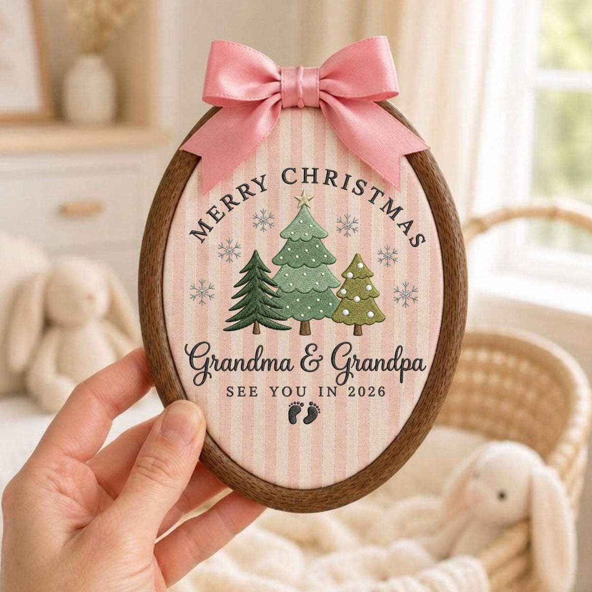 May include: An oval wooden embroidery hoop frame containing fabric with pink and white vertical stripes. The design features three green Christmas trees, snowflakes, and the text Merry Christmas Grandma &amp; Grandpa See You In 2026 with baby footprints. A pink satin bow is attached to the top.