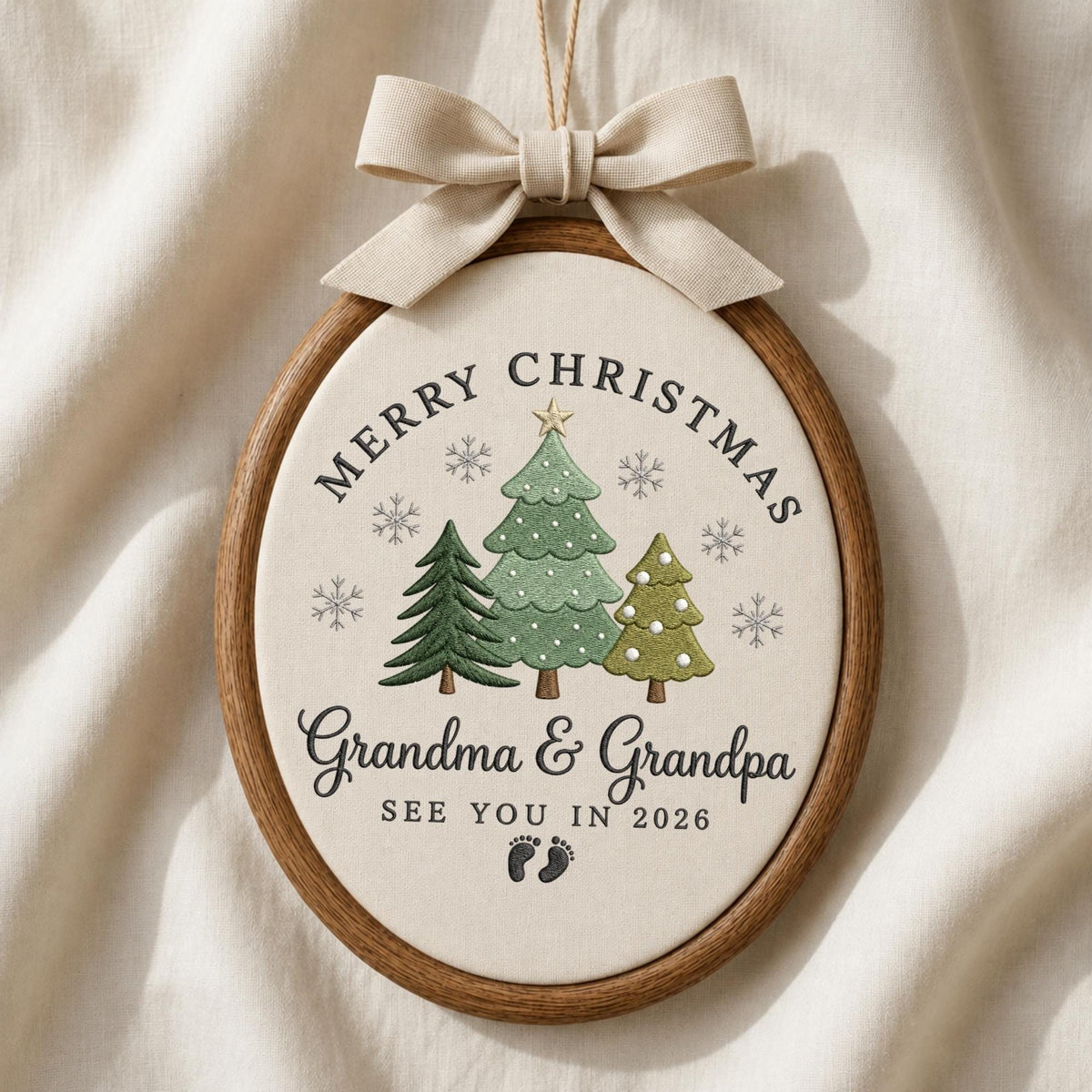 May include: An oval wooden embroidery hoop ornament featuring cream fabric with three embroidered green Christmas trees, snowflakes, and the text Merry Christmas Grandma &amp; Grandpa SEE YOU IN 2026 with baby footprints, topped with a beige ribbon bow.