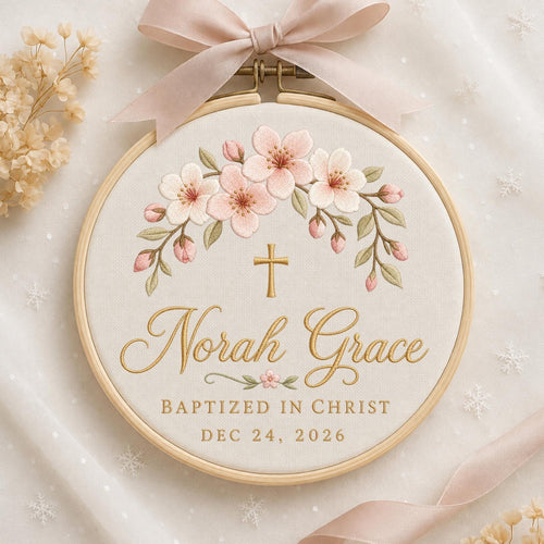 May include: A circular wooden embroidery hoop containing cream fabric with an embroidered arch of pink cherry blossoms and green leaves. A gold cross sits above the gold cursive text Norah Grace, BAPTIZED IN CHRIST, and DEC 24, 2026.