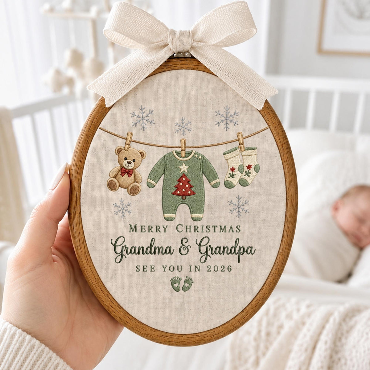 May include: An oval wooden embroidery hoop containing fabric with a printed design of a teddy bear, a green baby onesie with a red Christmas tree, and socks hanging on a line. Text reads: MERRY CHRISTMAS Grandma &amp; Grandpa SEE YOU IN 2026.