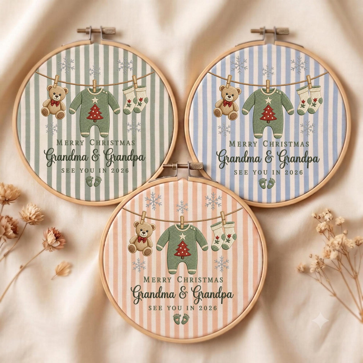 May include: Three circular embroidery hoops featuring striped fabric backgrounds in sage green, light blue, and soft peach. Each hoop displays a clothesline with a teddy bear, a baby onesie with a red Christmas tree, and socks, with the text MERRY CHRISTMAS Grandma &amp; Grandpa SEE YOU IN 2026.
