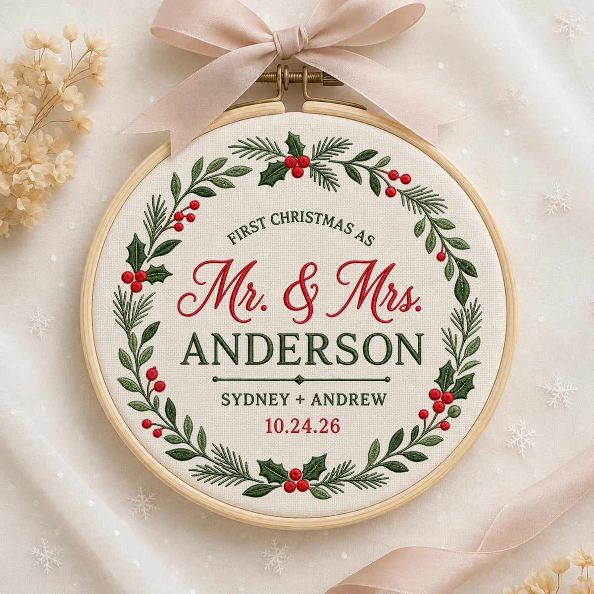 May include: A round wooden embroidery hoop containing white fabric with a festive wreath of green pine needles and red holly berries. The text reads: FIRST CHRISTMAS AS Mr. &amp; Mrs. ANDERSON SYDNEY + ANDREW 10.24.26. A light pink ribbon is tied at the top.