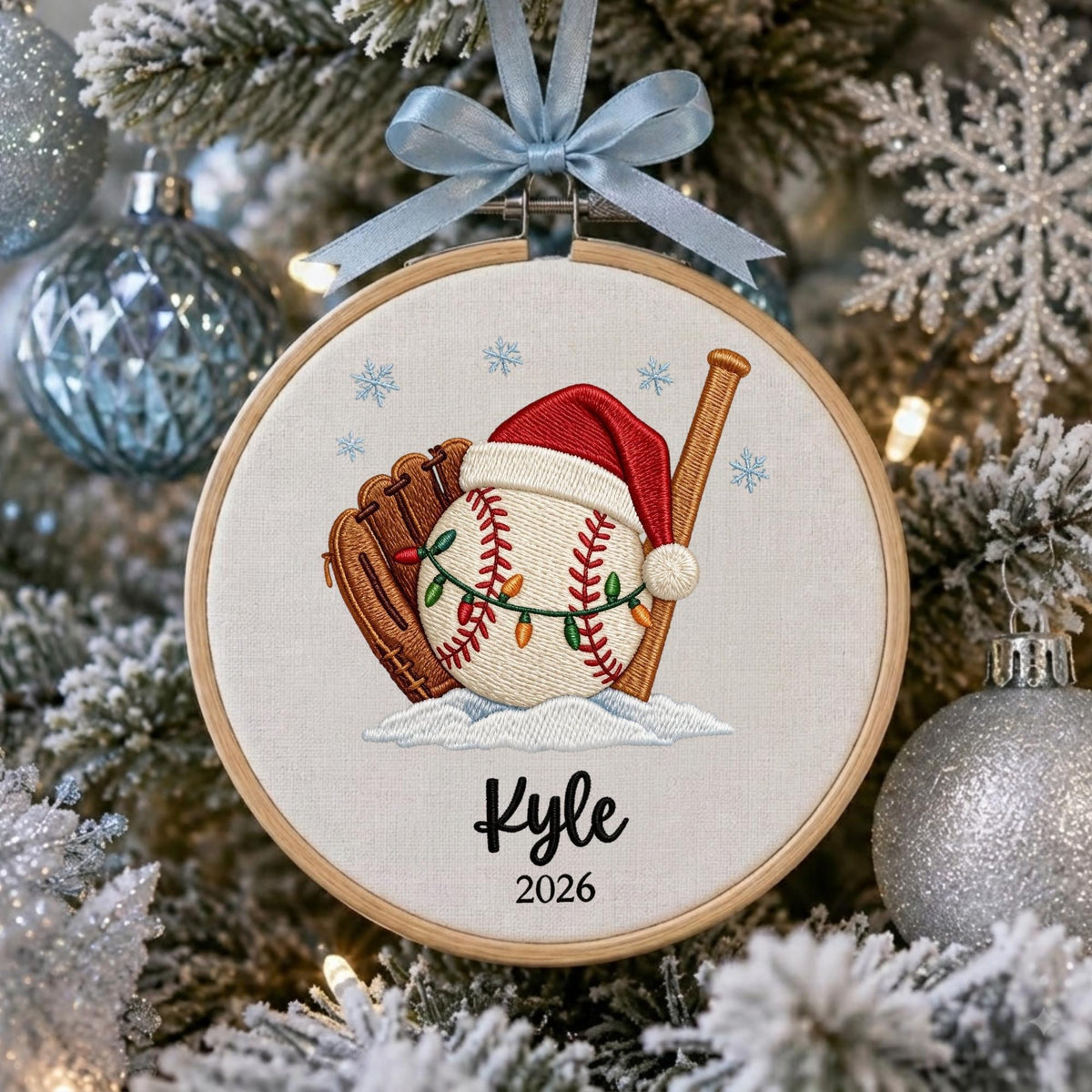 May include: A round wooden embroidery hoop ornament featuring a white fabric background with an embroidered baseball wearing a red Santa hat, a brown baseball glove, and a wooden bat. A string of colorful Christmas lights wraps around the baseball.