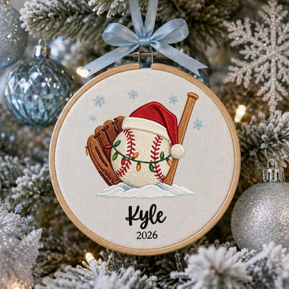 May include: A round wooden embroidery hoop ornament featuring a white fabric background with an embroidered baseball wearing a red Santa hat, a brown baseball glove, and a wooden bat. A string of colorful Christmas lights wraps around the baseball.