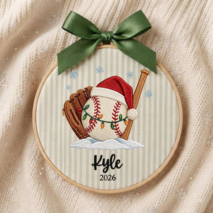 May include: A circular embroidery hoop featuring a baseball, a brown leather glove, and a wooden bat. The baseball wears a red Santa hat and is wrapped in colorful Christmas lights. The name Kyle and the year 2026 are stitched below. A green ribbon bow is attached to the top.
