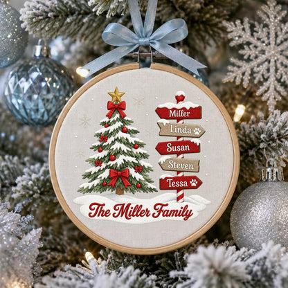 May include: A round wooden embroidery hoop ornament featuring a fabric center with a printed Christmas tree, red bows, and a signpost listing the names Miller, Linda, Susan, Steven, and Tessa. The text The Miller Family is printed below.