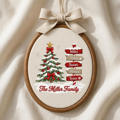 May include: An oval wooden embroidery hoop containing a fabric panel with a Christmas tree illustration, a signpost with the names Miller, Linda, Susan, Steven, and Tessa, and the text The Miller Family, topped with a beige fabric bow.