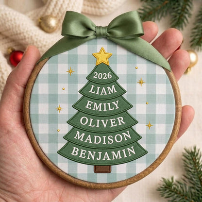 May include: A round wooden embroidery hoop ornament featuring a light green and white gingham fabric background. A green Christmas tree graphic is centered with a yellow star on top, the year 2026, and the names Liam, Emily, Oliver, Madison, Benjamin.