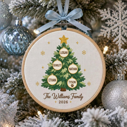 May include: A round wooden embroidery hoop ornament featuring a stitched green Christmas tree with a gold star. Five white circular ornaments hang on the tree with the names Logan, Scarlett, Nathan, Ethan, and Tyson. Text reads The Williams Family 2026.