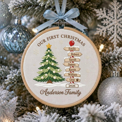 May include: A circular wooden embroidery hoop ornament featuring a stitched green Christmas tree with white ornaments and a yellow star. A signpost lists the names Emily, Robert, Sarah, James, Kevin, William, Orio, and the year 2026. Light blue ribbon.