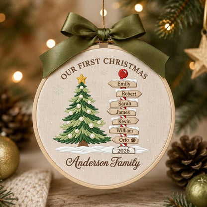 May include: A round embroidery hoop ornament featuring a beige fabric background with a green Christmas tree, a signpost with names Emily, Robert, Sarah, James, Kevin, William, Orio, and the text Our First Christmas and Anderson Family 2026.