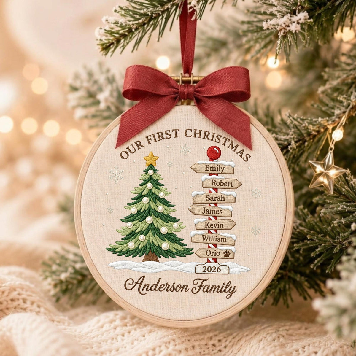 May include: A round embroidery hoop ornament featuring a green Christmas tree with a yellow star, a signpost with names Emily, Robert, Sarah, James, Kevin, William, Orio, and the text Our First Christmas, 2026, Anderson Family, topped with a red bow.