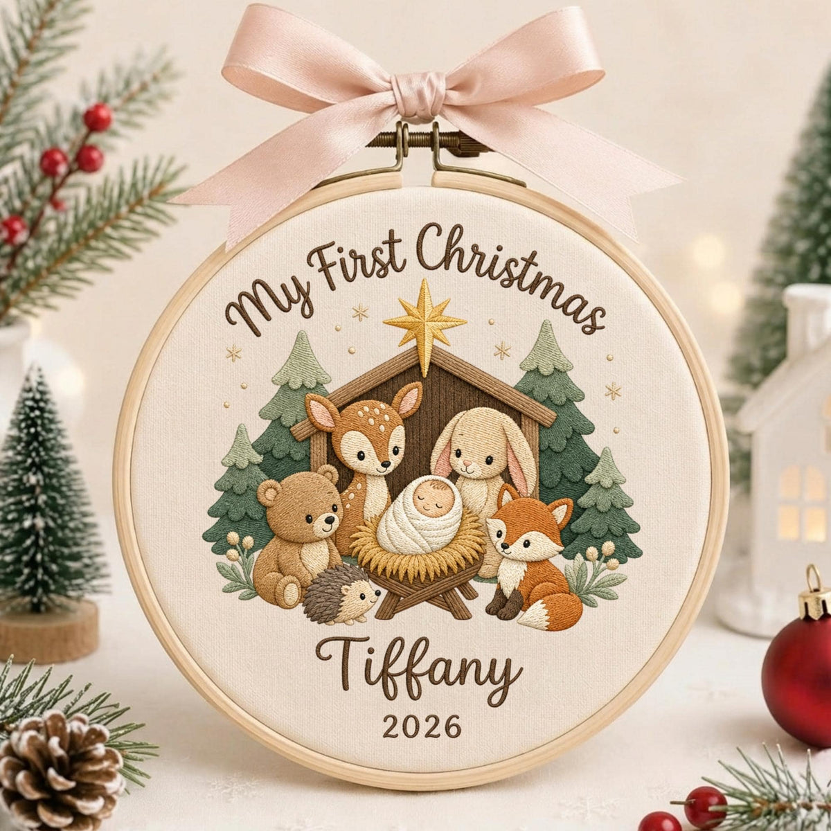 May include: A round wooden embroidery hoop featuring a cream fabric background with the text My First Christmas, Tiffany, and 2026. The design shows a manger with a baby, a bear, a deer, a rabbit, a hedgehog, and a fox, topped with a pink ribbon.