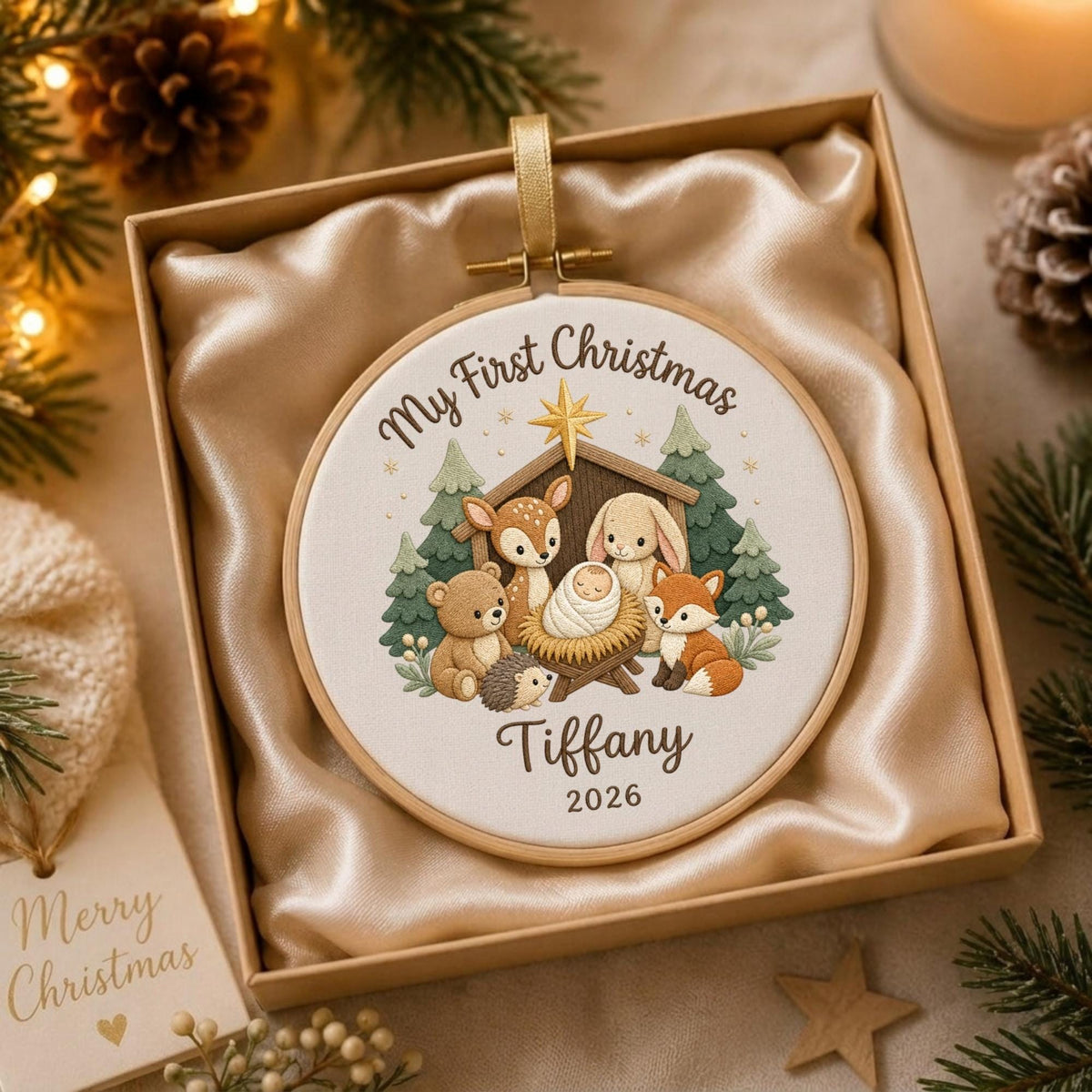 May include: A round embroidery hoop ornament featuring a white fabric center with a printed illustration of a baby in a manger surrounded by a deer, rabbit, bear, hedgehog, and fox. Text reads My First Christmas, Tiffany, and 2026.