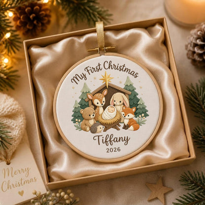 May include: A round embroidery hoop ornament featuring a white fabric center with a printed illustration of a baby in a manger surrounded by a deer, rabbit, bear, hedgehog, and fox. Text reads My First Christmas, Tiffany, and 2026.