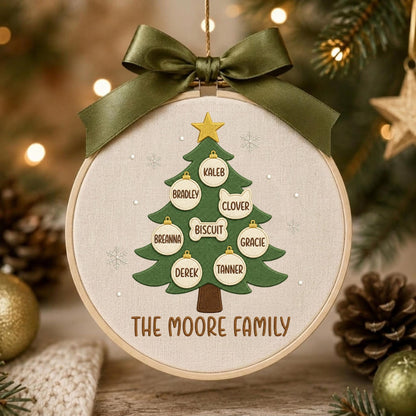 May include: A circular embroidery hoop ornament featuring a green fabric Christmas tree with a yellow star on top. The tree is decorated with white ornaments labeled with the names Kaleb, Bradley, Clover, Biscuit, Breanna, Gracie, Derek, and Tanner. The text THE MOORE FAMILY is embroidered below the tree, and an olive green ribbon bow is attached to the top.