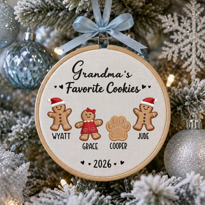 May include: A round wooden embroidery hoop ornament featuring the embroidered text Grandma's Favorite Cookies. It includes two gingerbread figures wearing Santa hats, a gingerbread figure in a red dress, and a paw print, with the names Wyatt, Grace, and Cooper, plus the year 2026. A light blue ribbon is tied at the top.