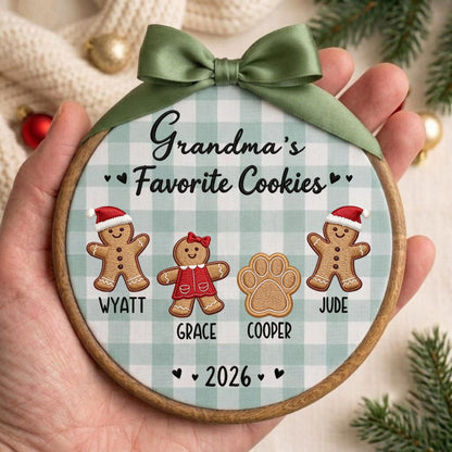 May include: A round wooden embroidery hoop ornament featuring a light green and white buffalo check fabric background. It displays the text Grandma's Favorite Cookies, gingerbread figures named Wyatt and Jude, a girl gingerbread, a paw print named Cooper, and 2026.
