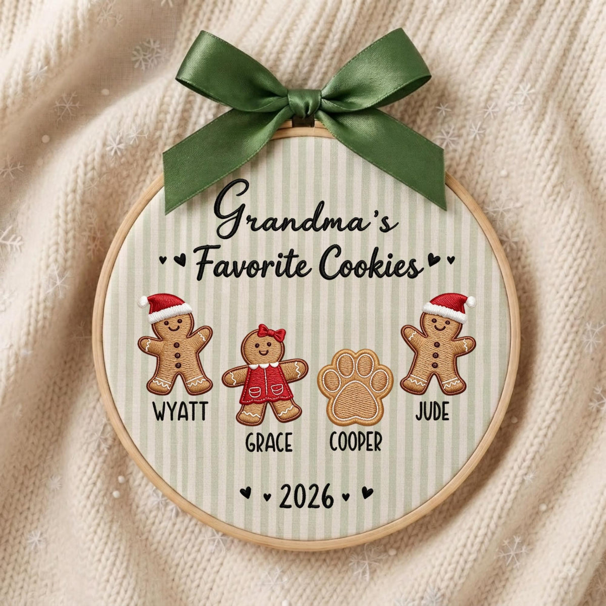 May include: A round embroidery hoop featuring the text Grandma's Favorite Cookies and the year 2026. It displays two gingerbread figures wearing red hats, one gingerbread figure in a red dress, and one paw print, with names Wyatt, Grace, and Cooper below.