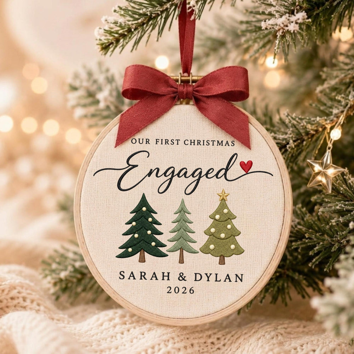May include: A round wooden embroidery hoop ornament featuring cream fabric with the text OUR FIRST CHRISTMAS Engaged and a red heart. Below are three embroidered Christmas trees in varying shades of green, with SARAH &amp; DYLAN 2026 printed below.