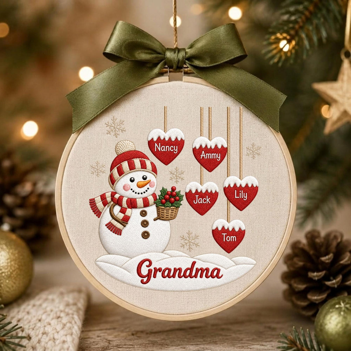 May include: A round wooden embroidery hoop ornament featuring a white snowman with a red and white striped hat and scarf, holding a basket of holly. Five red heart-shaped tags hang above with the names Nancy, Ammy, Jack, Lily, and Tom.