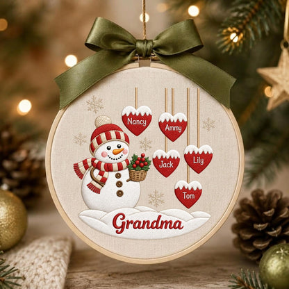 May include: A round wooden embroidery hoop ornament featuring a white snowman with a red and white striped hat and scarf, holding a basket of holly. Five red heart-shaped tags hang above with the names Nancy, Ammy, Jack, Lily, and Tom.