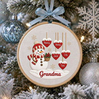 May include: A round wooden embroidery hoop ornament featuring a snowman wearing a red and white striped hat and scarf. Five red heart-shaped ornaments hang above, labeled Nancy, Ammy, Jack, Lily, and Tom. The word Grandma is printed below.